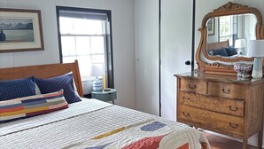 Un dormitorio con cama, cómoda, espejo, ventana y ventilador de techo.