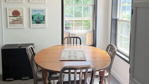 Un comedor con una mesa redonda de madera, cuatro sillas, una lámpara colgante negra y cuadros en la pared.