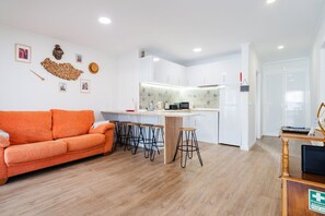 Een moderne woonkamer met een bank, een keuken met een bar, en een eettafel met krukken.