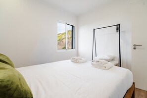 Ein Schlafzimmer mit einem Bett, einem Fenster mit Blick auf eine felsige Landschaft, einem schwarzen Metallbettgestell und einer Tür mit Griff.