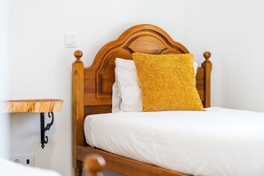 A bed with a wooden headboard, white bedding, and a yellow textured pillow. - GuestReady - Casa Avó Celeste (Faial)