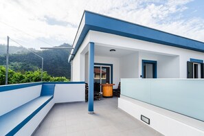Ein modernes Gebäude mit Flachdach, einem Balkon mit blauen Geländern und Blick auf eine gebirgige Landschaft.