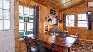 Um quarto com painéis de madeira, uma grande mesa, cadeiras, uma janela com cortinas e um letreiro com a inscrição 'The Caterpillar Place'.