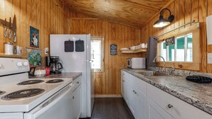Uma cozinha com paredes de madeira, fogão, geladeira e diversos utensílios.