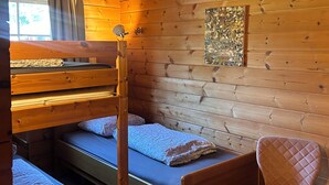 A cabin interior with a bunk bed, a single bed, a chair, and a window with curtains. - Scandinavian Bungalow with a Veranda on the Water! (Hulshorst)
