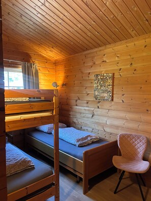 A cabin interior with a bunk bed, a single bed, a chair, and a window with curtains. - Scandinavian Bungalow with a Veranda on the Water! (Hulshorst)