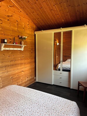 Ein Schlafzimmer mit Holzbalkendecke, einem Bett mit Blumenmuster und einem Kleiderschrank sowie einem kleinen Tisch.
