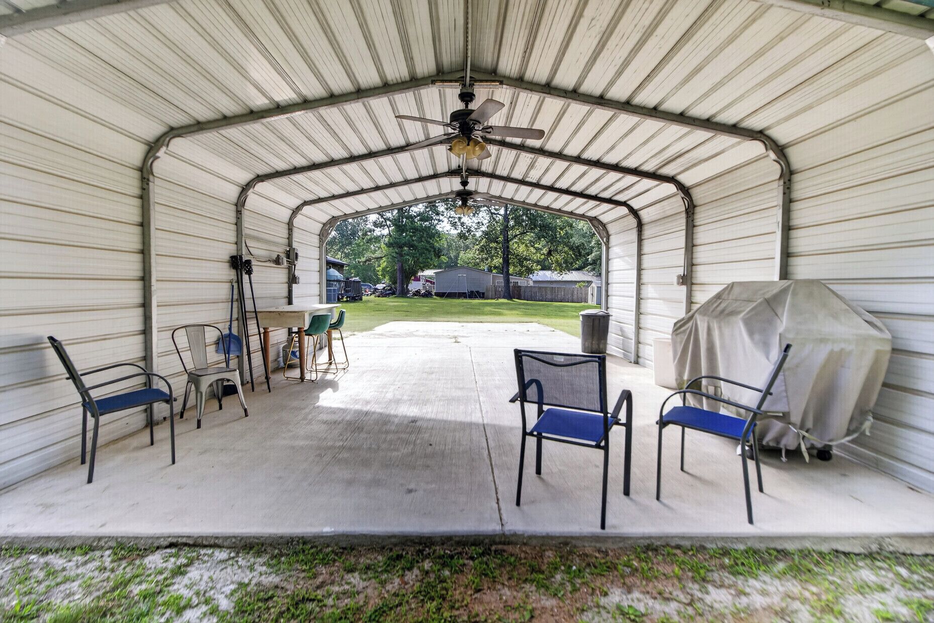 A covered patio with chairs, a table, and a ceiling fan.