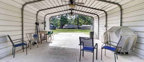 A covered patio with chairs, a table, and a ceiling fan.