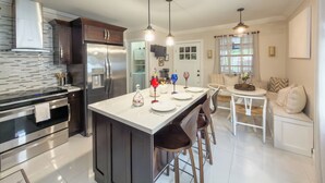 A modern kitchen with a central island, stainless steel appliances, pendant lighting, and a dining area with a white table and chairs. - Wynwood/Midtown Retreat–Walk to Miami Attractions! (Miami)