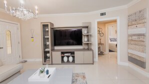 A modern living room with a large flat-screen TV, a chandelier, a white sofa, and a coffee table. - Wynwood/Midtown Retreat–Walk to Miami Attractions! (Miami)