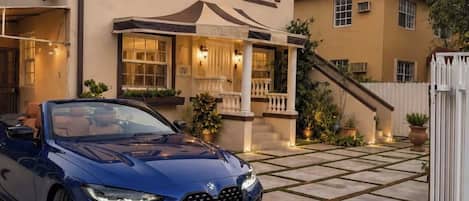 Una casa de dos pisos con un porche cubierto y un coche azul estacionado frente.