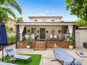 Ein zweistöckiges Haus mit überdachter Terrasse, Sitzgelegenheiten im Freien und einer Hängematte.