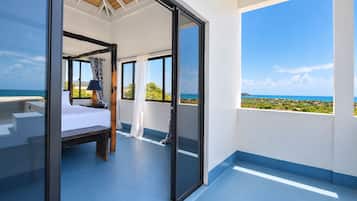 A bedroom with a bed, a nightstand, and a window with a view of the ocean.