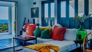 Ein modernes Wohnzimmer mit einer Couch, bunten Kissen, einem Couchtisch und Blick ins Freie.