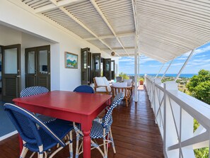 Un espacio al aire libre techado con piso de madera, una mesa roja y sillas de mimbre.