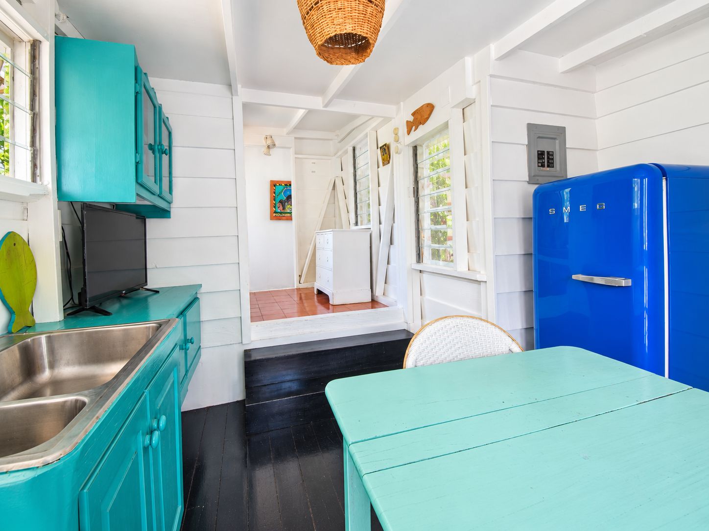 A kitchen with teal cabinets, a blue refrigerator, and a dining area with a teal table.