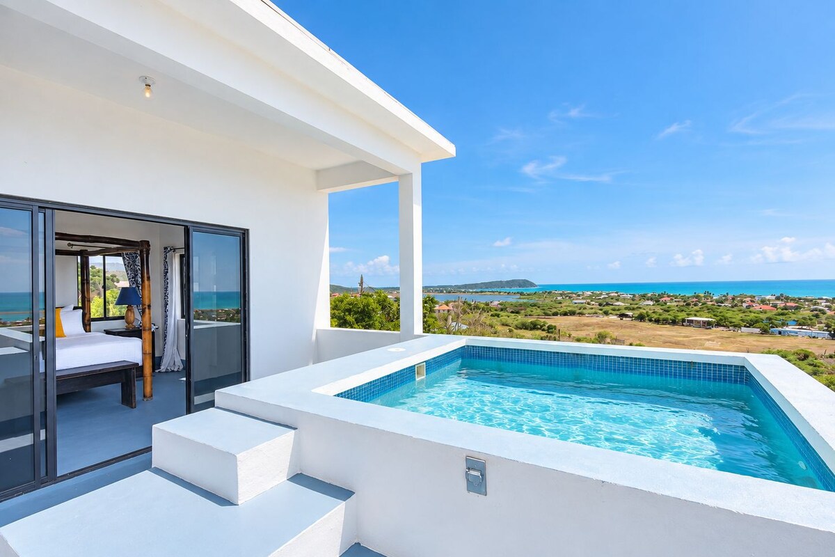 A modern hotel room with a balcony, a hot tub, and a view of the sea and landscape.