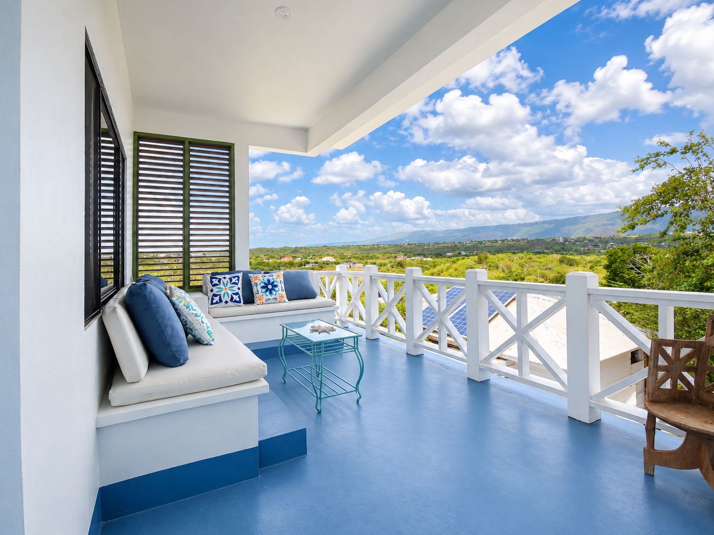 A balcony with a white railing, a seating area with cushions, and a view of the landscape.