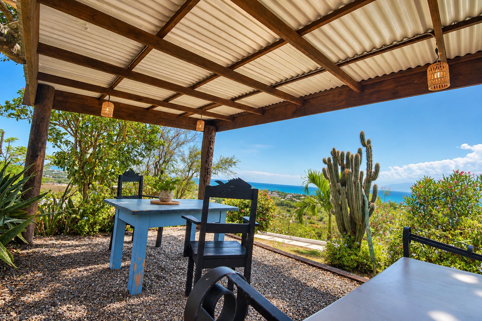 Un patio exterior con una mesa y sillas, vista al océano y un cactus al fondo.