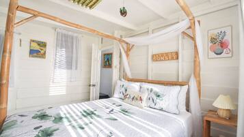 A room with a bed under a bamboo canopy, a wall with a 'Let's Do Sunset' sign, and a framed picture of birds.