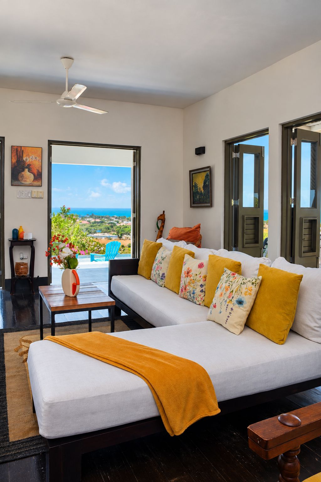 Un moderno salón con un sofá blanco, un cojín amarillo y vistas al océano.
