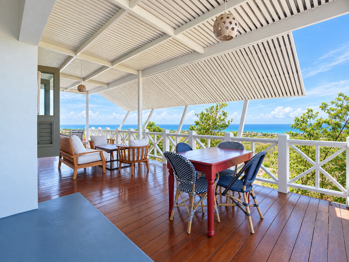 A covered outdoor seating area with a wooden table and chairs, overlooking a scenic ocean view.