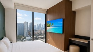 Une chambre d’hôtel avec un grand lit, un bureau, une chaise, un téléviseur fixé au mur et une vue sur le paysage urbain.