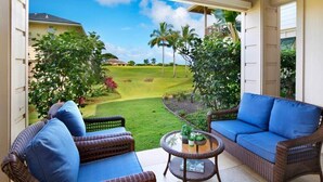 A patio with wicker furniture, a round table, and a view of a golf course. - Pili Mai at Poipu - Condo on Kiahuna Golf Course - Pool, Spa, AC, Walk to Beach (Koloa)