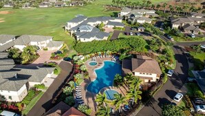 A residential area with a central swimming pool surrounded by houses, a golf course in the background, and a clear sky. - Pili Mai at Poipu - Condo on Kiahuna Golf Course - Pool, Spa, AC, Walk to Beach (Koloa)