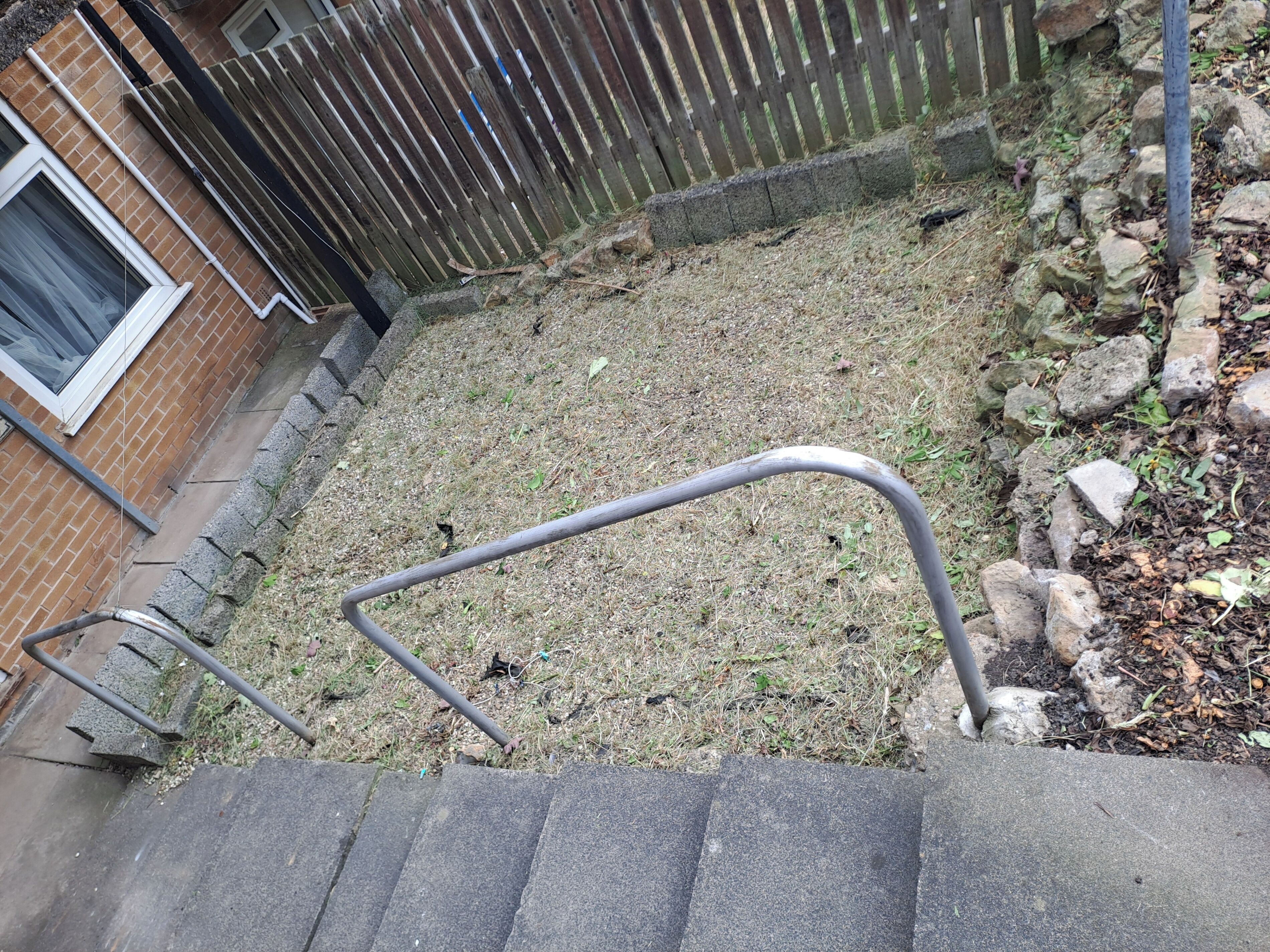 Een betonnen trap die leidt naar een grasveld, met een houten omheining en een bakstenen muur op de achtergrond.