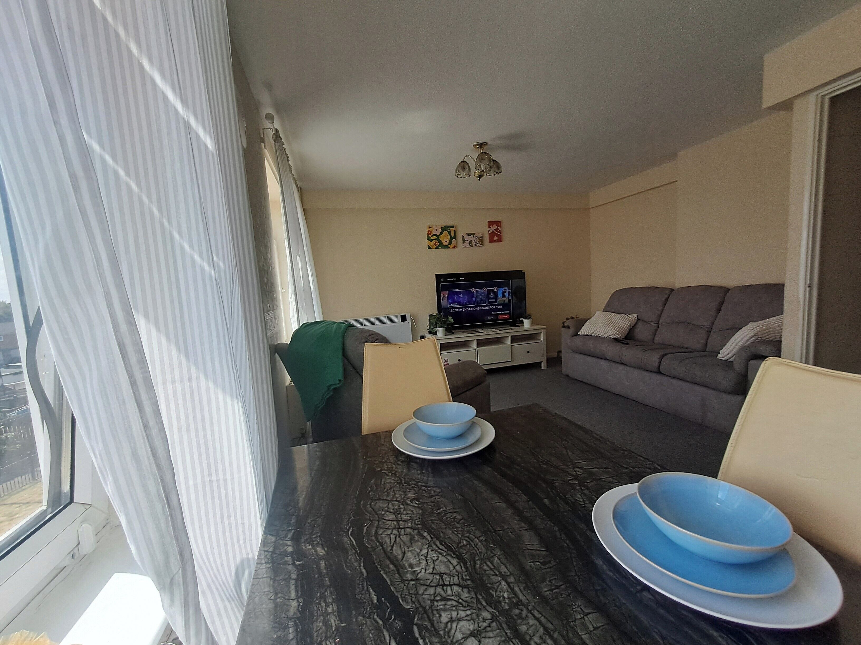 Un salon avec un canapé, un téléviseur, une table avec des bols et une fenêtre avec des rideaux.