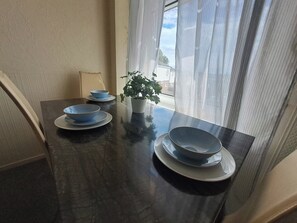 A dining table with plates and bowls, a potted plant, and a window with curtains. - Apartment Sleeps 5 With Parking (Nottingham)