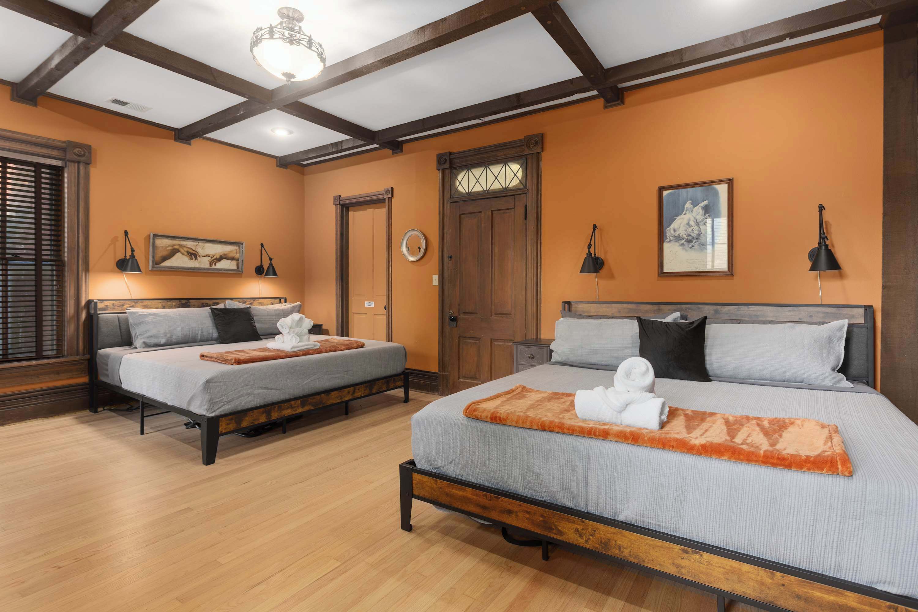 Habitación de hotel con dos camas, vigas de madera en el techo, una puerta de madera y obras de arte en las paredes.