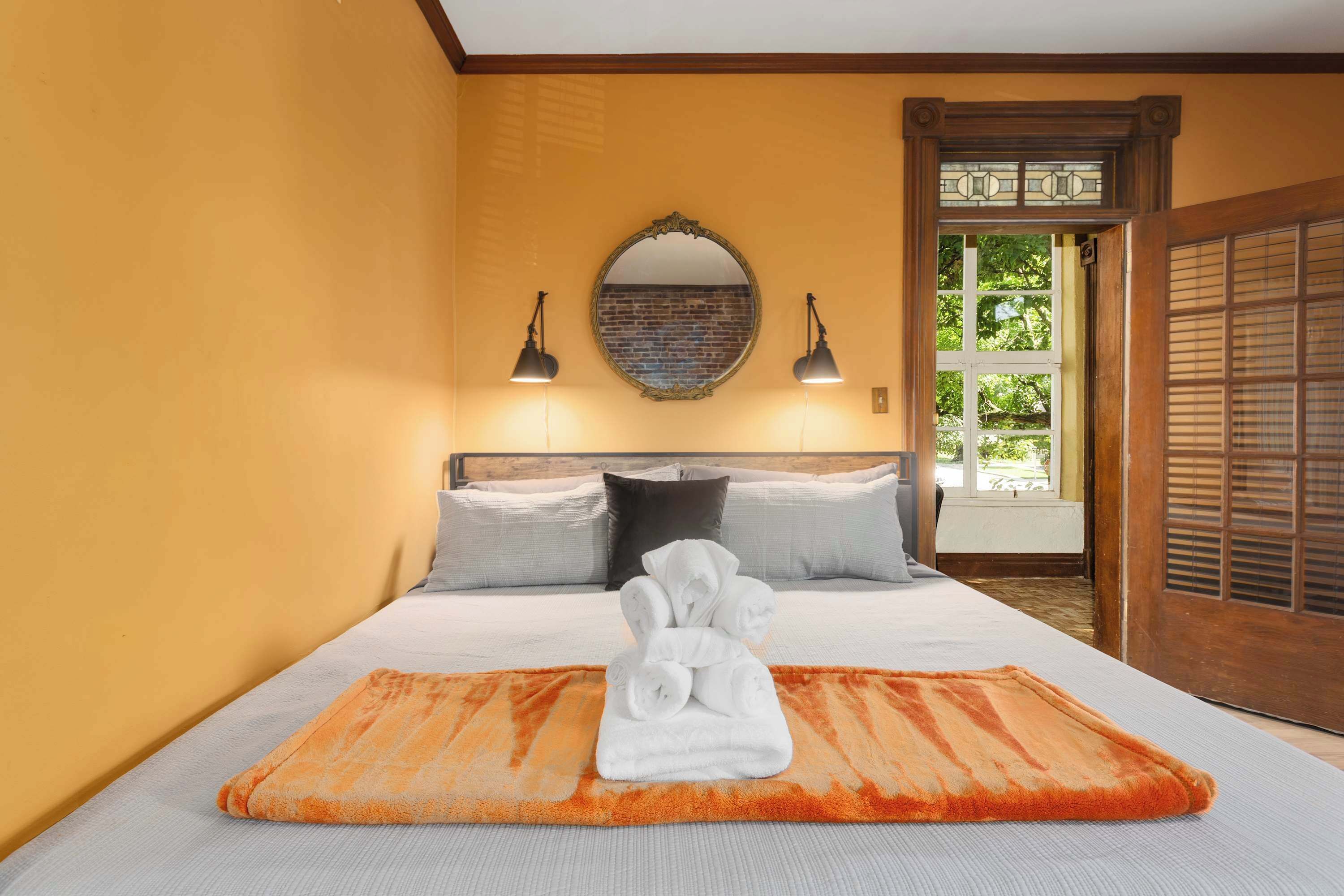 Un dormitorio con cama, almohadas, un espejo y una ventana.