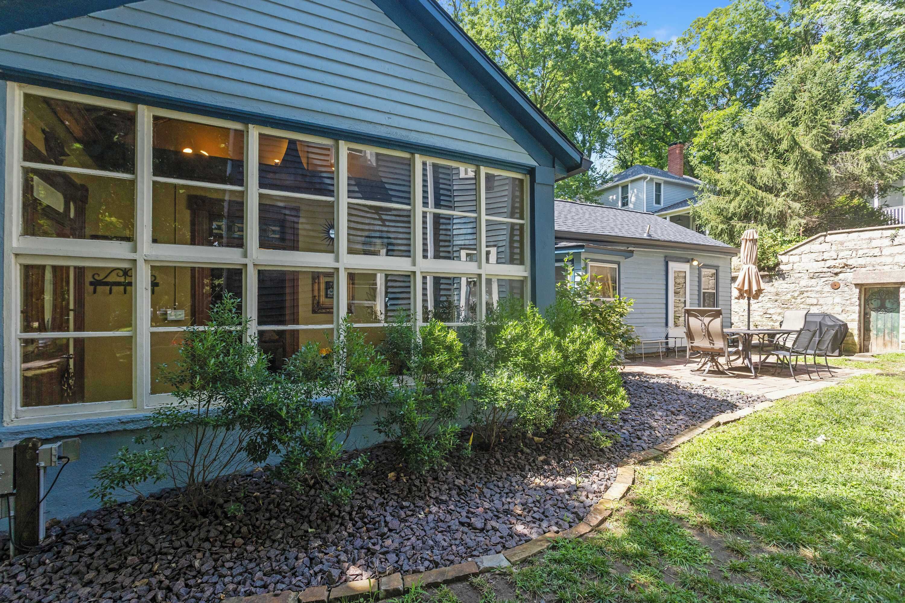 A house with large windows, a patio with outdoor furniture, and a stone wall.