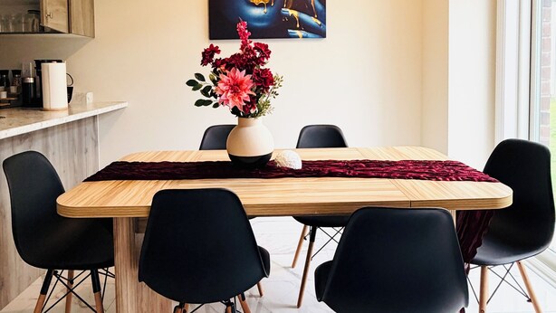 Ein Essbereich mit Marmorboden, einem Holztisch, schwarzen Stühlen, einer Vase mit Blumen und einem Gemälde an der Wand.