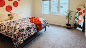 Ein Schlafzimmer mit Bett, Fenster, Spiegel und Wandbildern.
