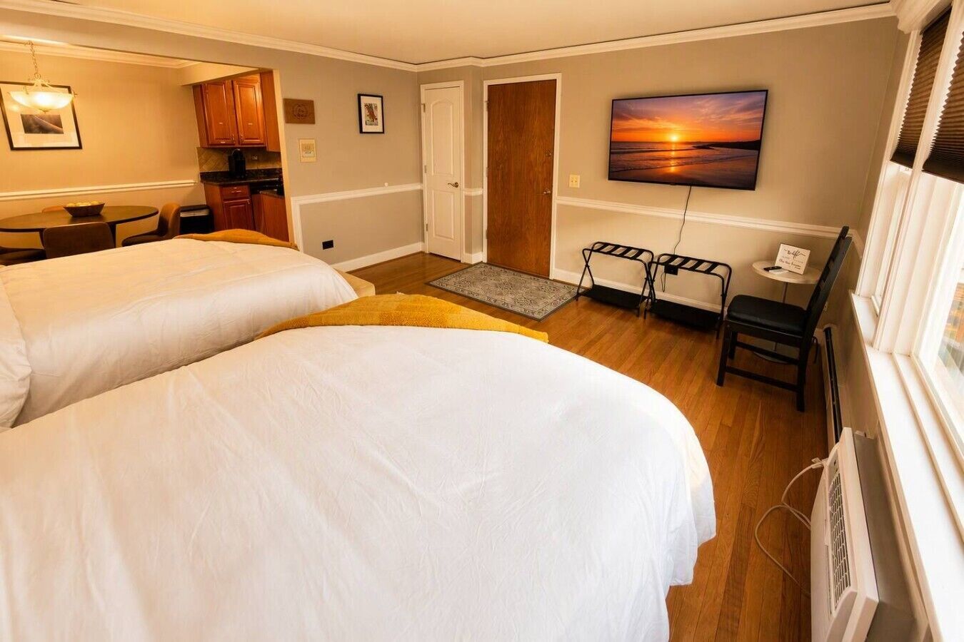 A hotel room with two beds, a desk, a chair, a TV, and a painting on the wall.