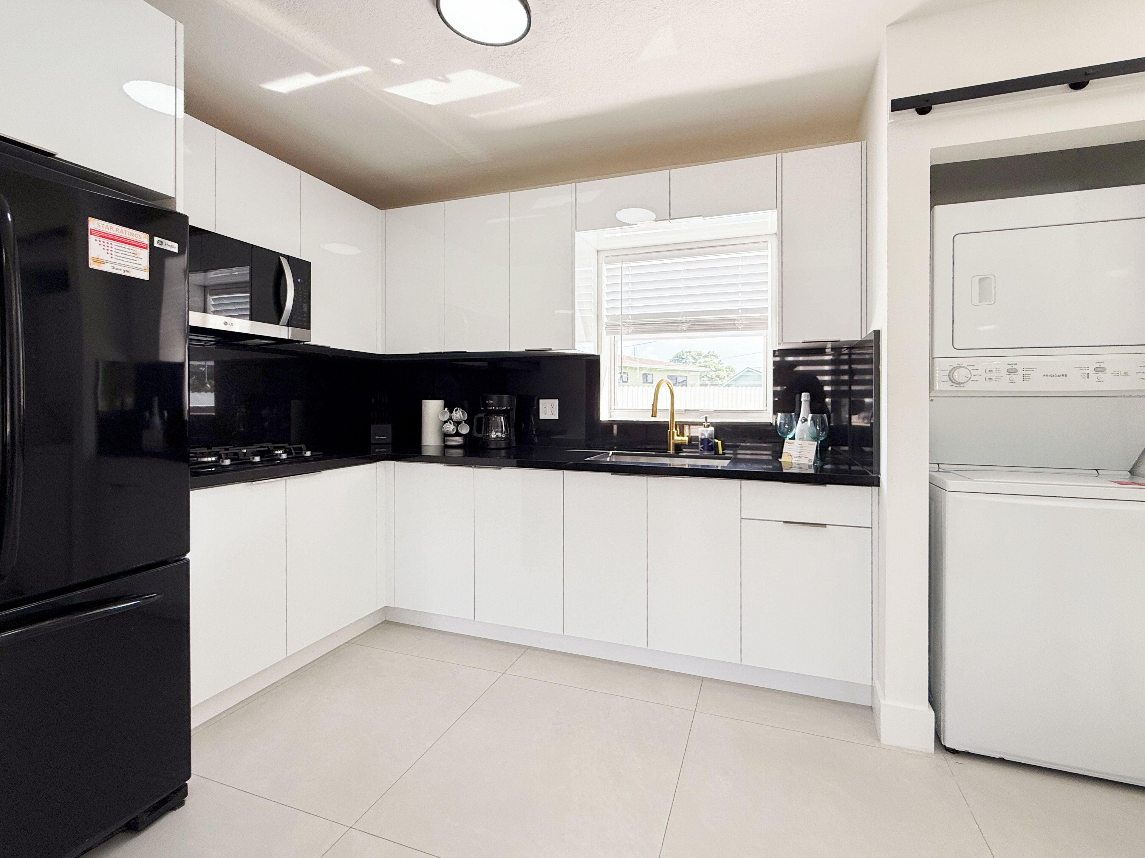 Eine moderne Küche mit weißen Schränken, einem schwarzen Kühlschrank, einer Mikrowelle, einer Kaffeemaschine und einem Geschirrspüler.