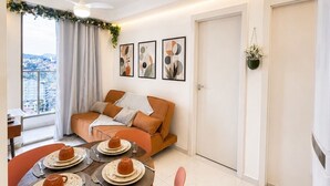 Un salon moderne avec un canapé, une table à manger dressée pour deux personnes et une vue sur la ville par la fenêtre.