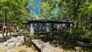 Una cabaña de madera rústica con una mesa de picnic y una parrilla, rodeada de árboles y rocas.