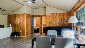 Interior de una cabaña con comedor, cama y vista por una ventana.