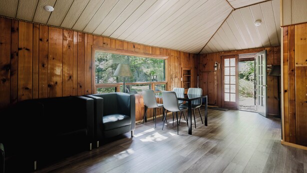 Un interior de madera con un sofá, sillas, una mesa y un ventanal.