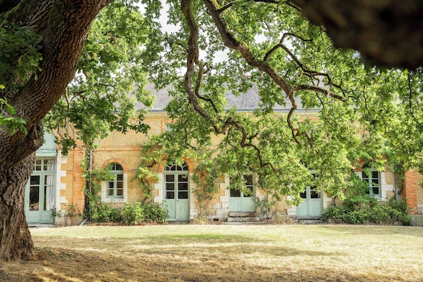 A building with arched windows and a brick facade, surrounded by a grassy area and a large tree.