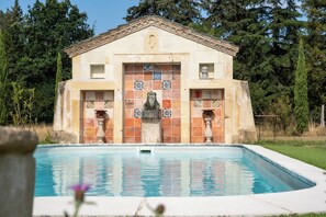 Un edificio con fachada de tejas, una piscina en primer plano y un paisaje natural al fondo.