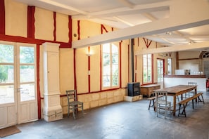 A spacious room with a large wooden table and benches, a fireplace, and a kitchen area with a counter and cabinets.