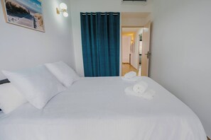 Hotellihuone, jossa on sänky, valkoiset tyynyt, sininen verho ja pyyhkeet sängyllä.