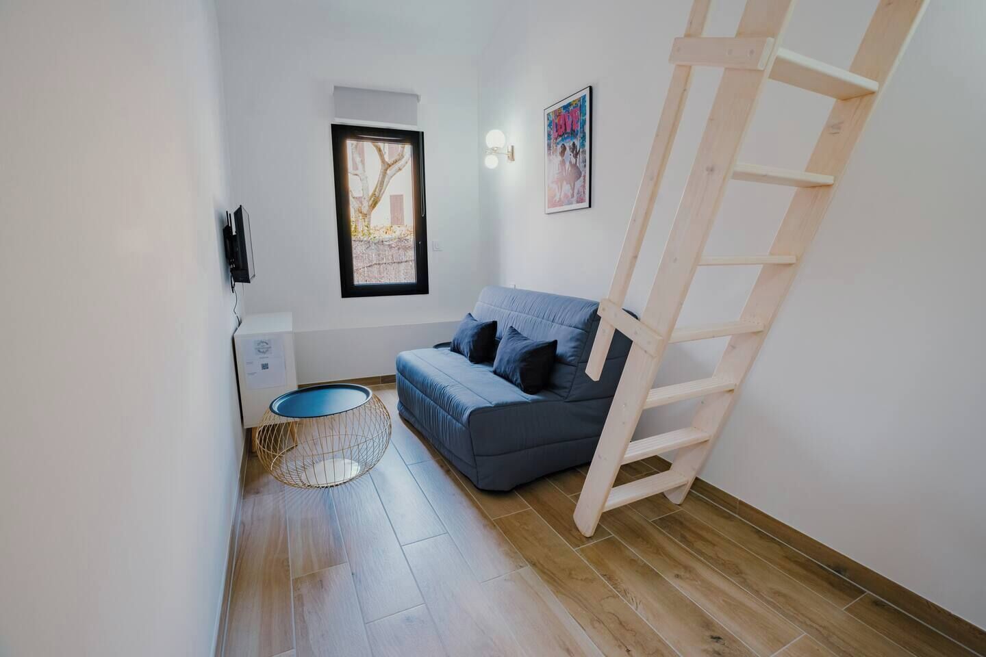 Un petit espace de vie moderne, avec un canapé bleu, une table basse ronde et une échelle en bois.