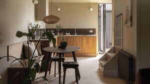 Una cuina moderna amb taulell de fusta, una zona de menjador amb taula rodona i tamborets, i una escala que mena a una planta superior.